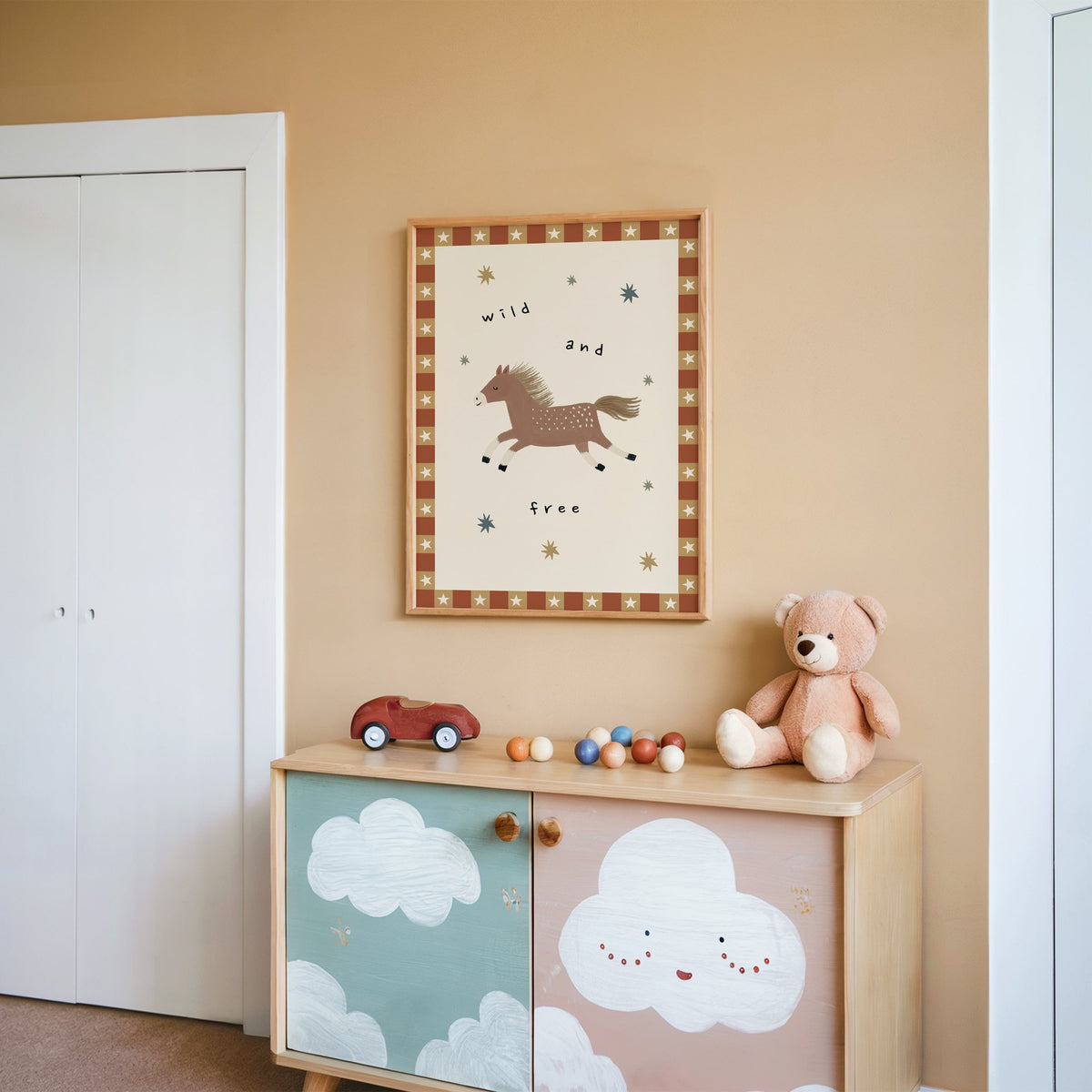 Wild and free pony nursery print in an oak frame on a peach wall above a cloud-painted cabinet