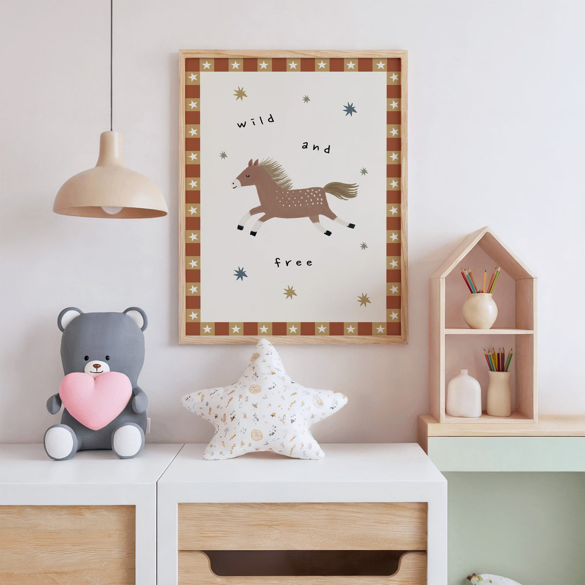 Wild and free pony nursery print in an oak frame above a white dresser with a star pillow and house shelf