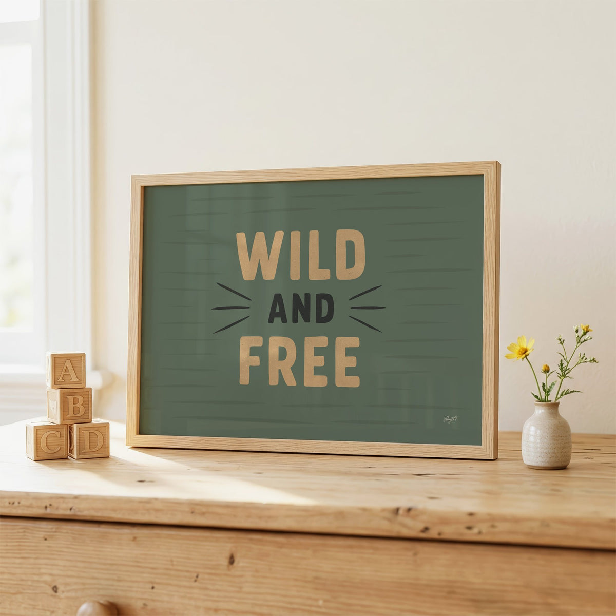 Wild and free sage green quote nursery print in an oak frame on a wooden dresser beside ABC blocks