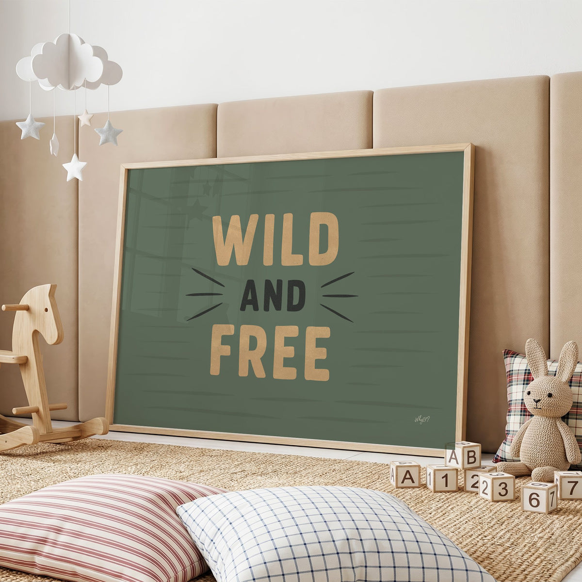 Wild and free sage green quote nursery print in an oak frame on a padded wall by a wooden rocking horse