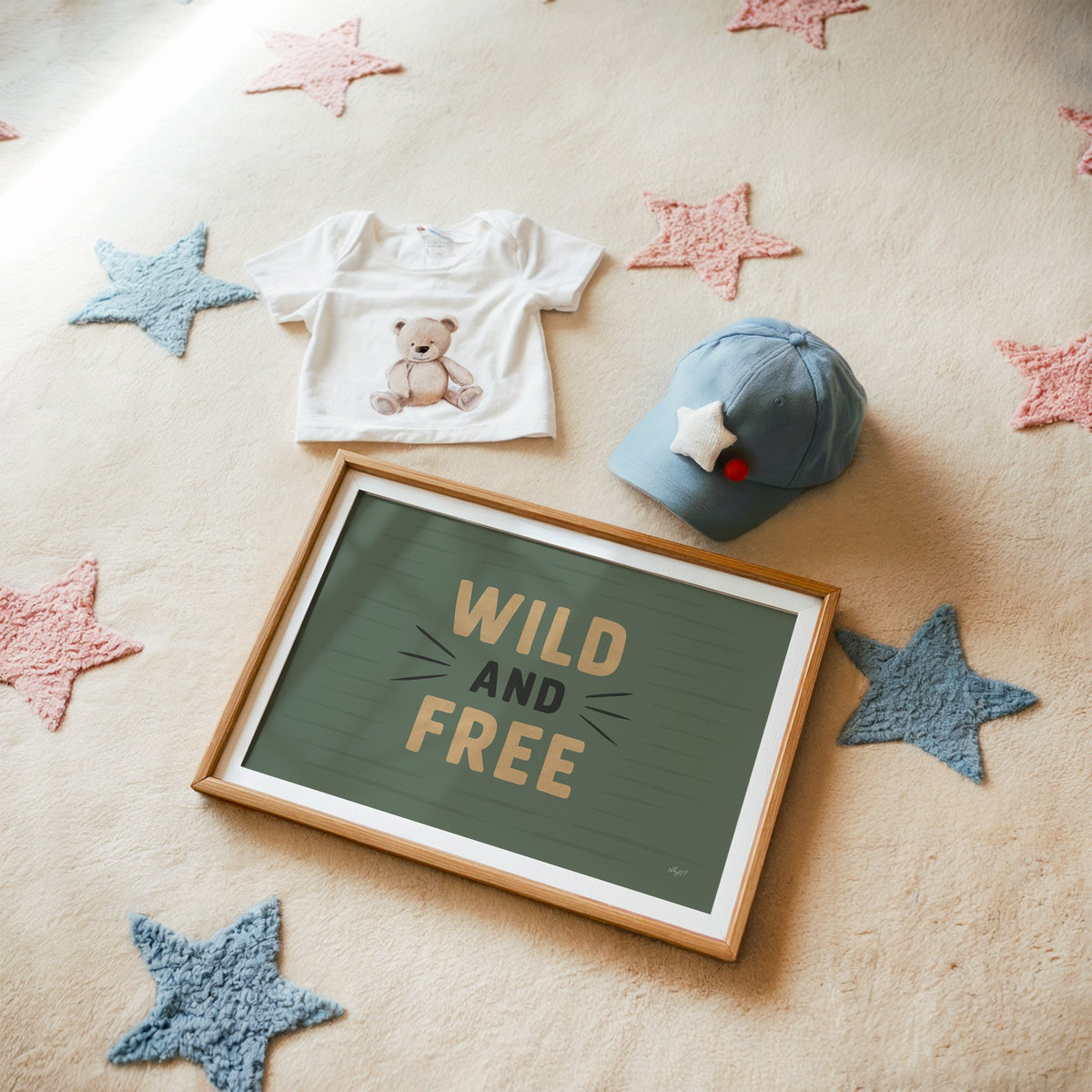 Wild and free sage green quote nursery print in a matted oak frame on a star rug with a baby tee