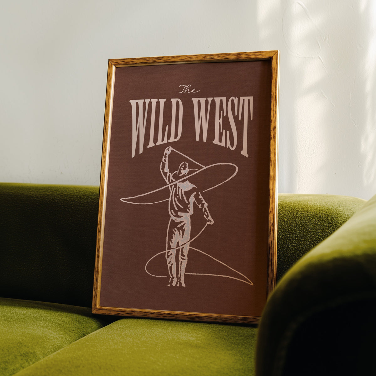 The Wild West lasso brown print in an oak frame leaning on a green velvet sofa