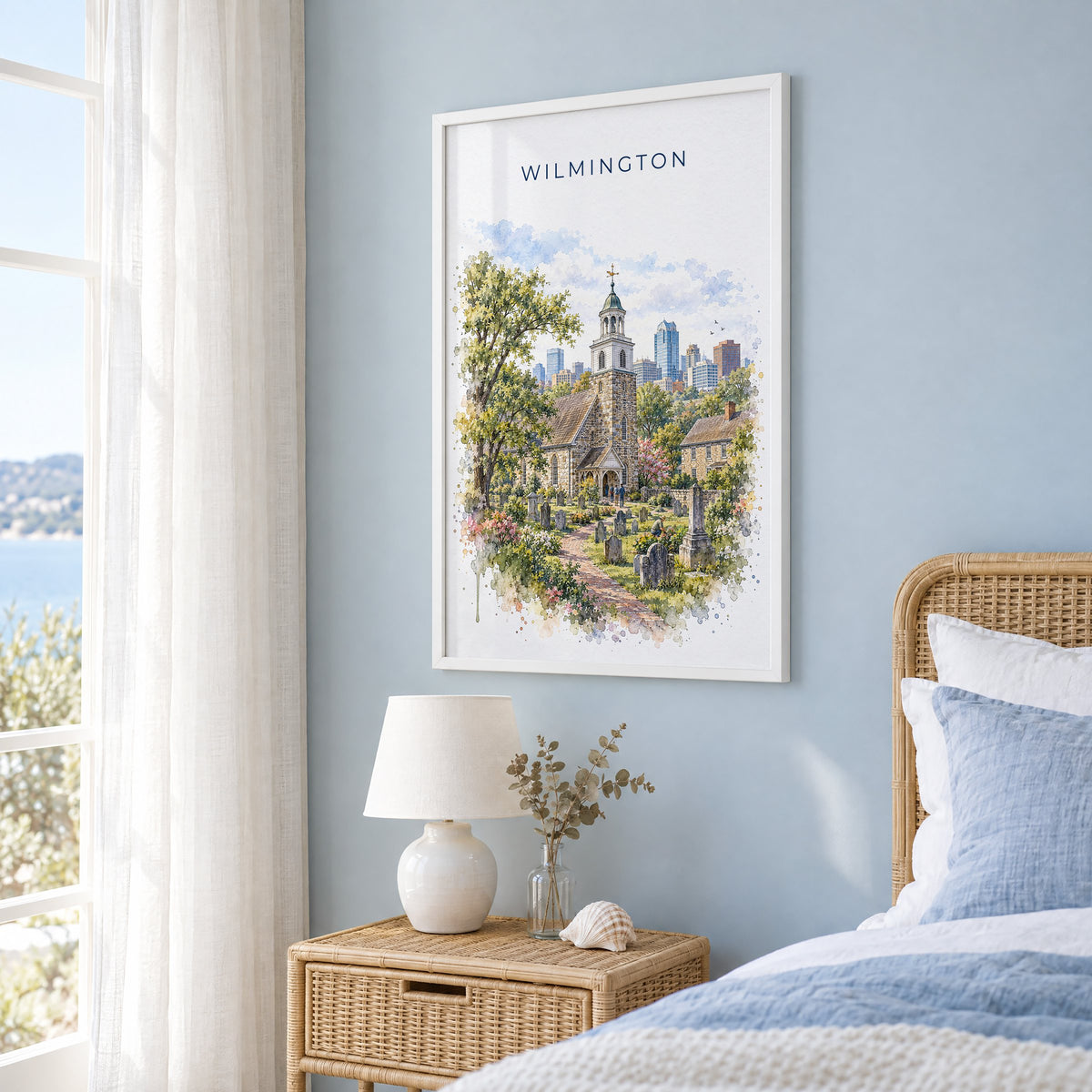 Wilmington, Delaware watercolor print in a white frame on a pale blue wall beside a rattan bed in a coastal bedroom