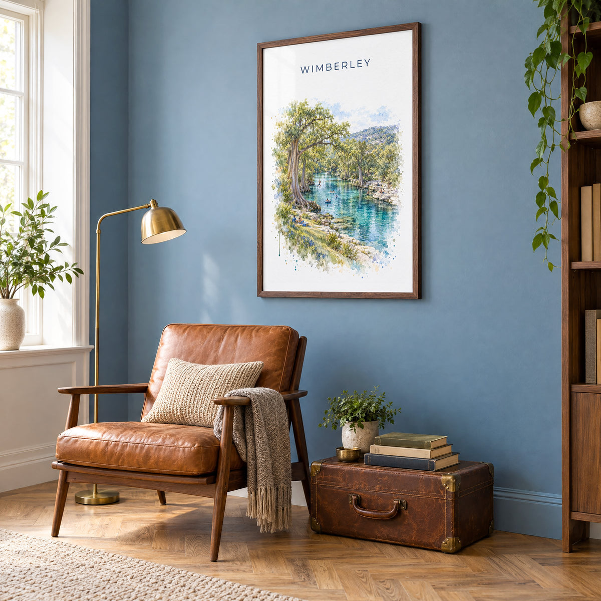 Wimberley, Texas watercolor print in a walnut frame on a blue wall above a leather armchair in a reading nook
