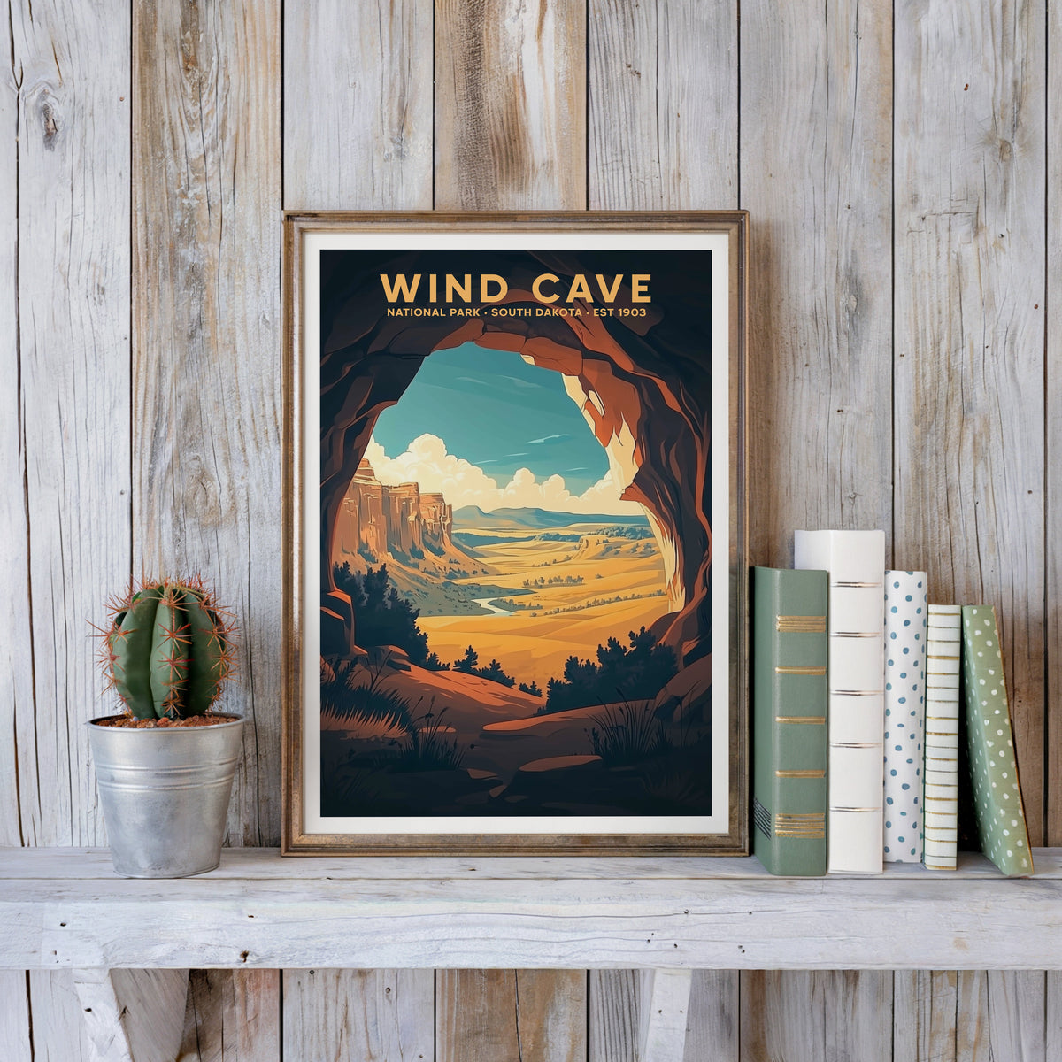 Wind Cave poster in an antique gold frame against whitewashed farmhouse planks beside books and a cactus