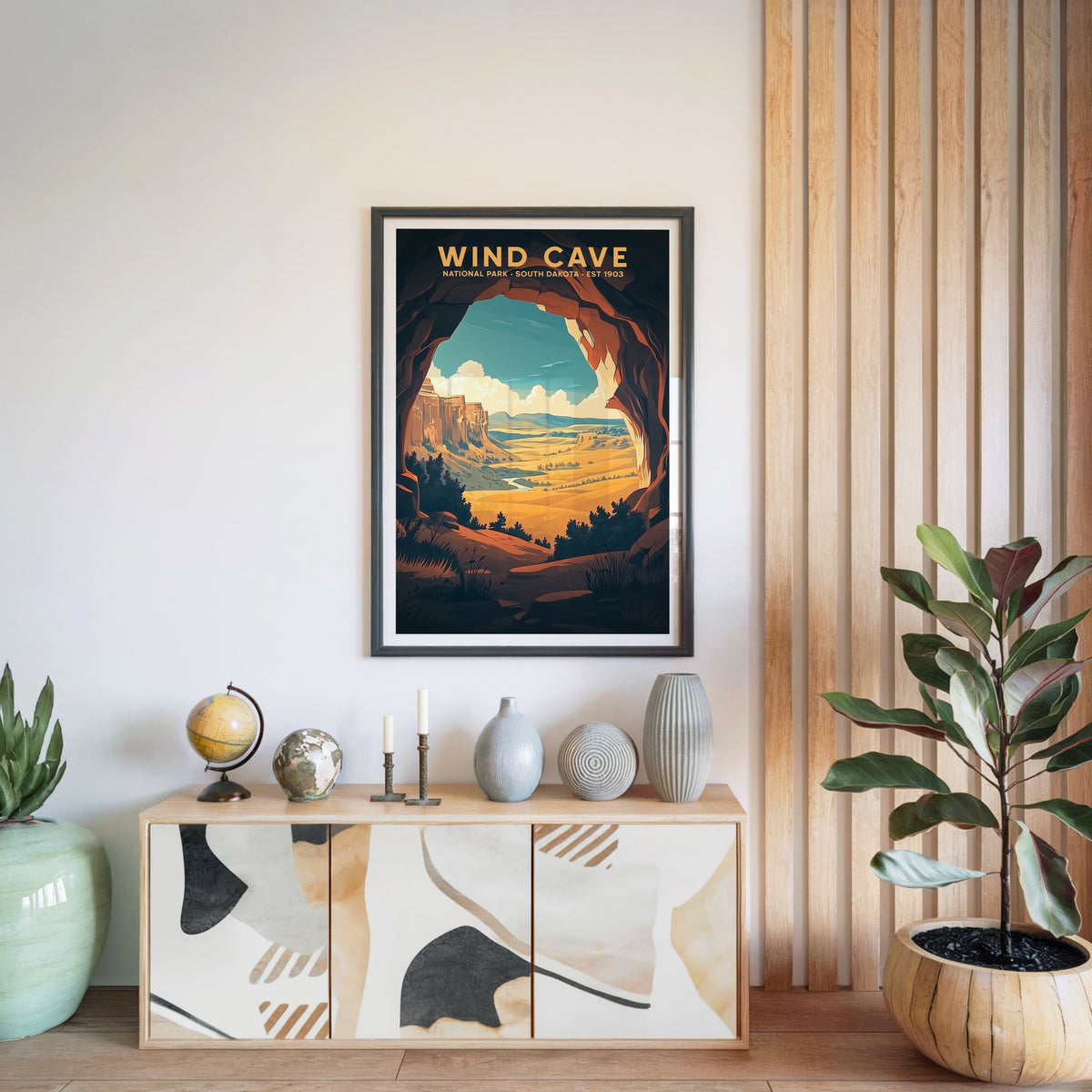 Wind Cave National Park print in a black frame above a light wood sideboard with a globe and ceramic vases