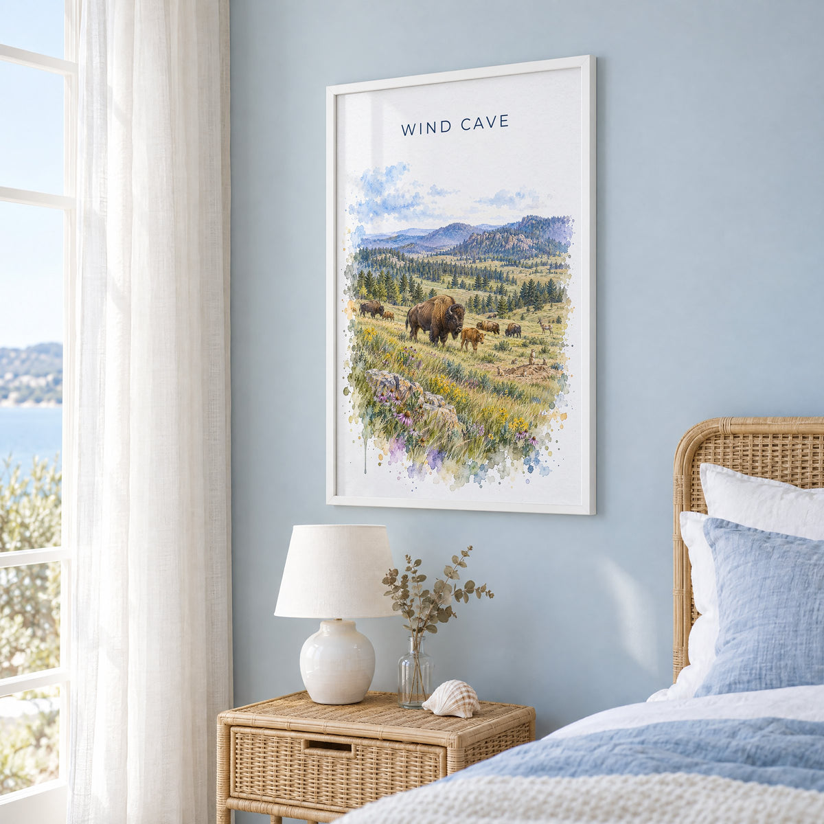 Wind Cave National Park watercolor print in a white frame on a pale blue wall beside a rattan bed in a coastal bedroom