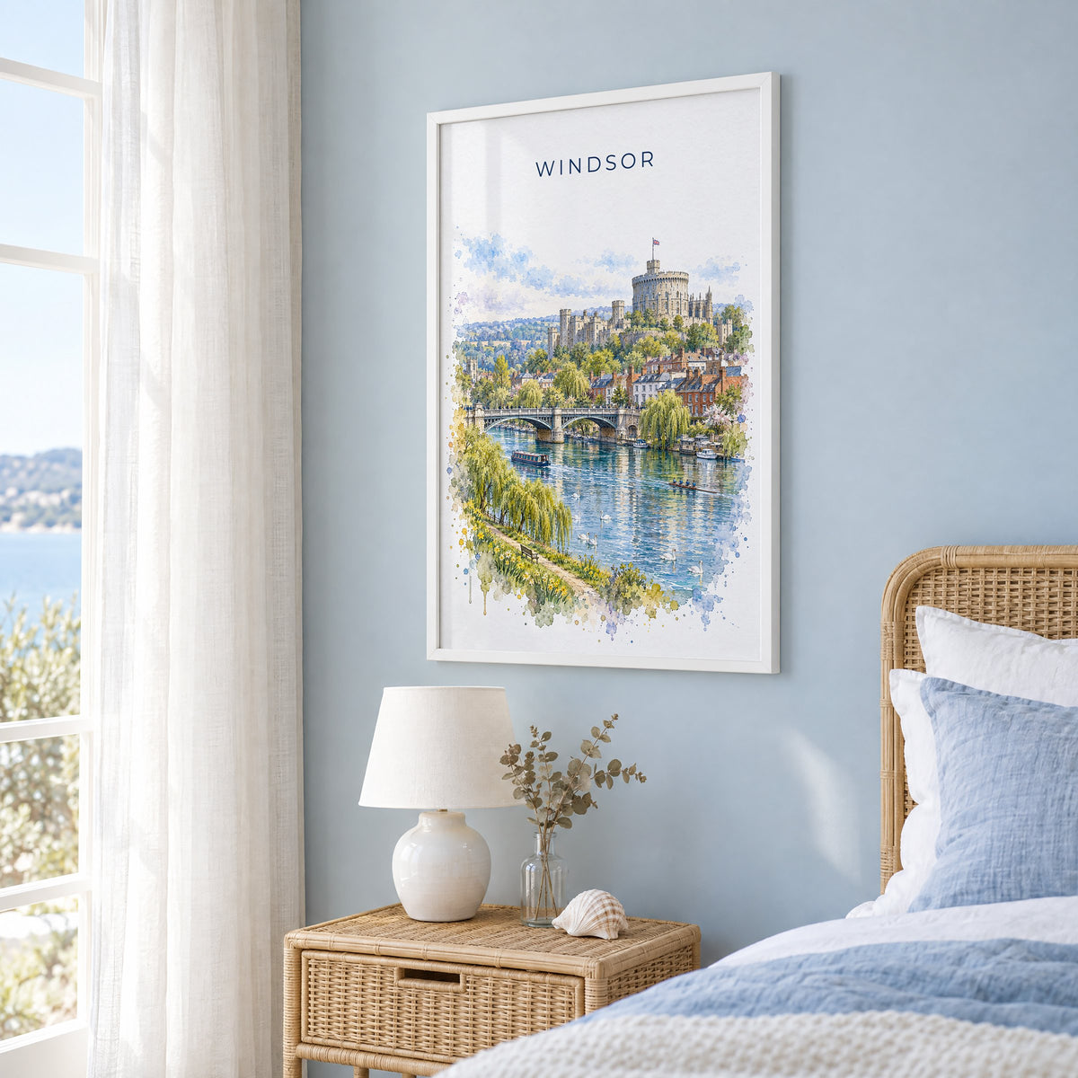 Windsor, England watercolor print in a white frame on a pale blue wall beside a rattan bed in a coastal bedroom