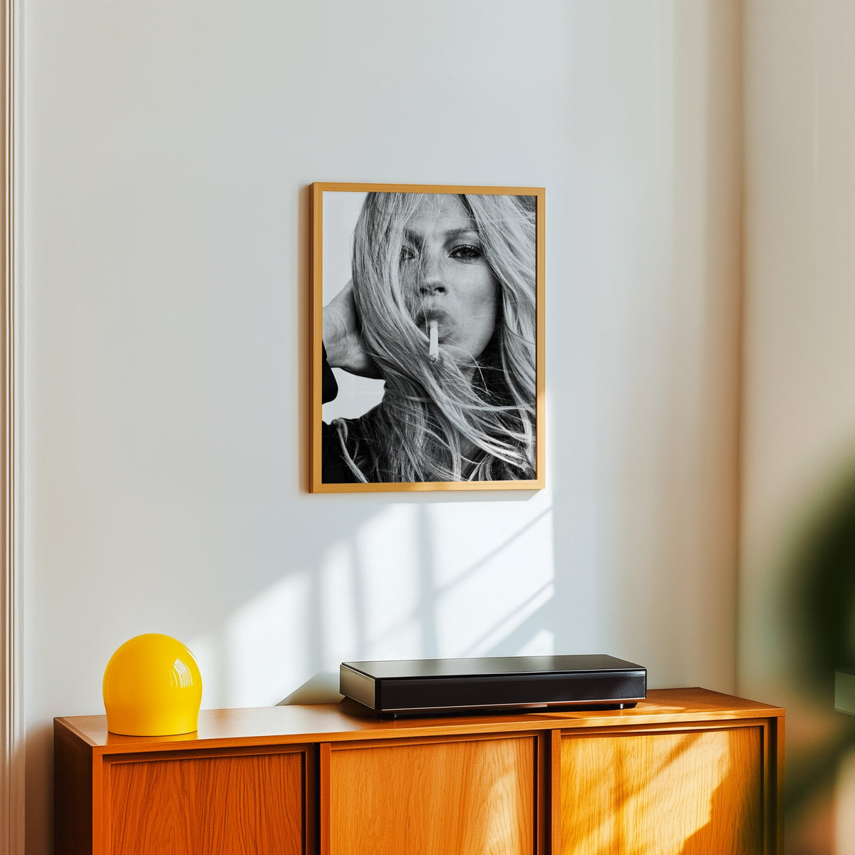 Woman with windswept hair across her face print in an oak frame above a teak sideboard with a yellow glass lamp