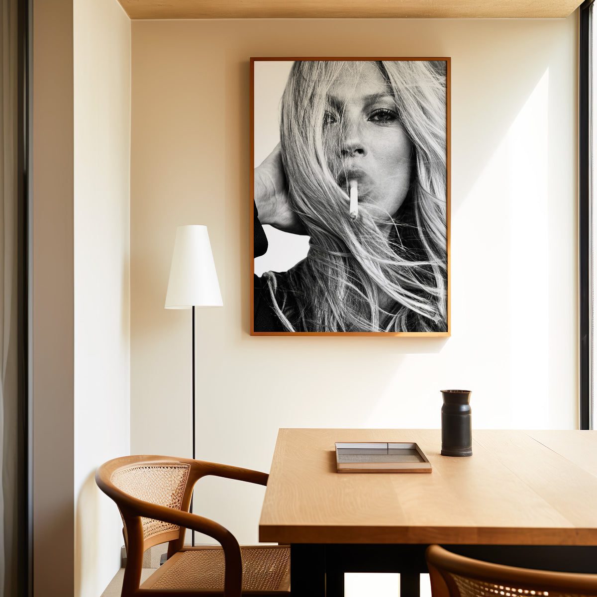 Woman with windswept hair across her face print in an oak frame above a dining table and cane chair
