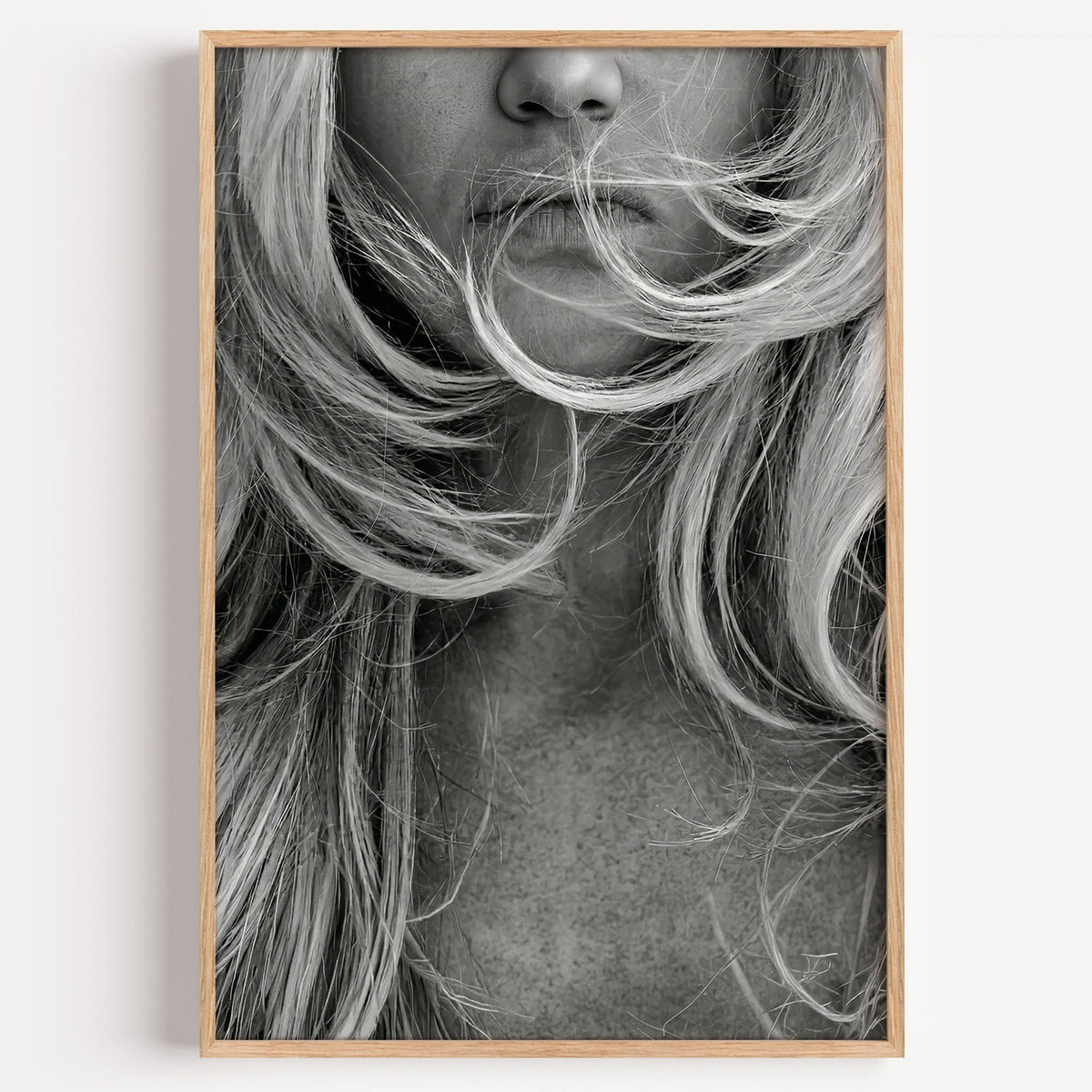 Windswept blonde hair over lips closeup print in a light oak frame on a plain white wall