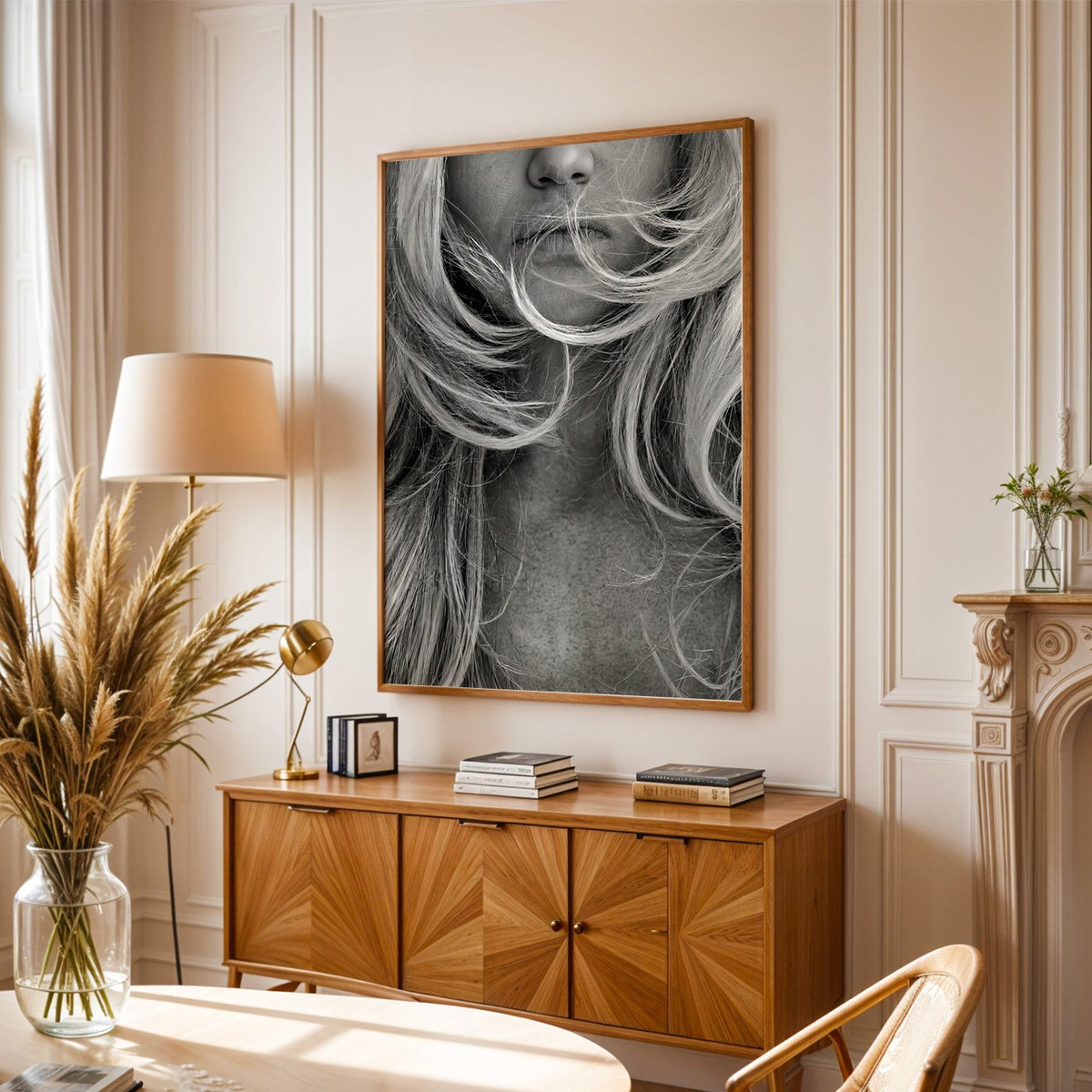 Windswept blonde hair over lips closeup print in an oak frame above a sunburst wood sideboard with pampas grass
