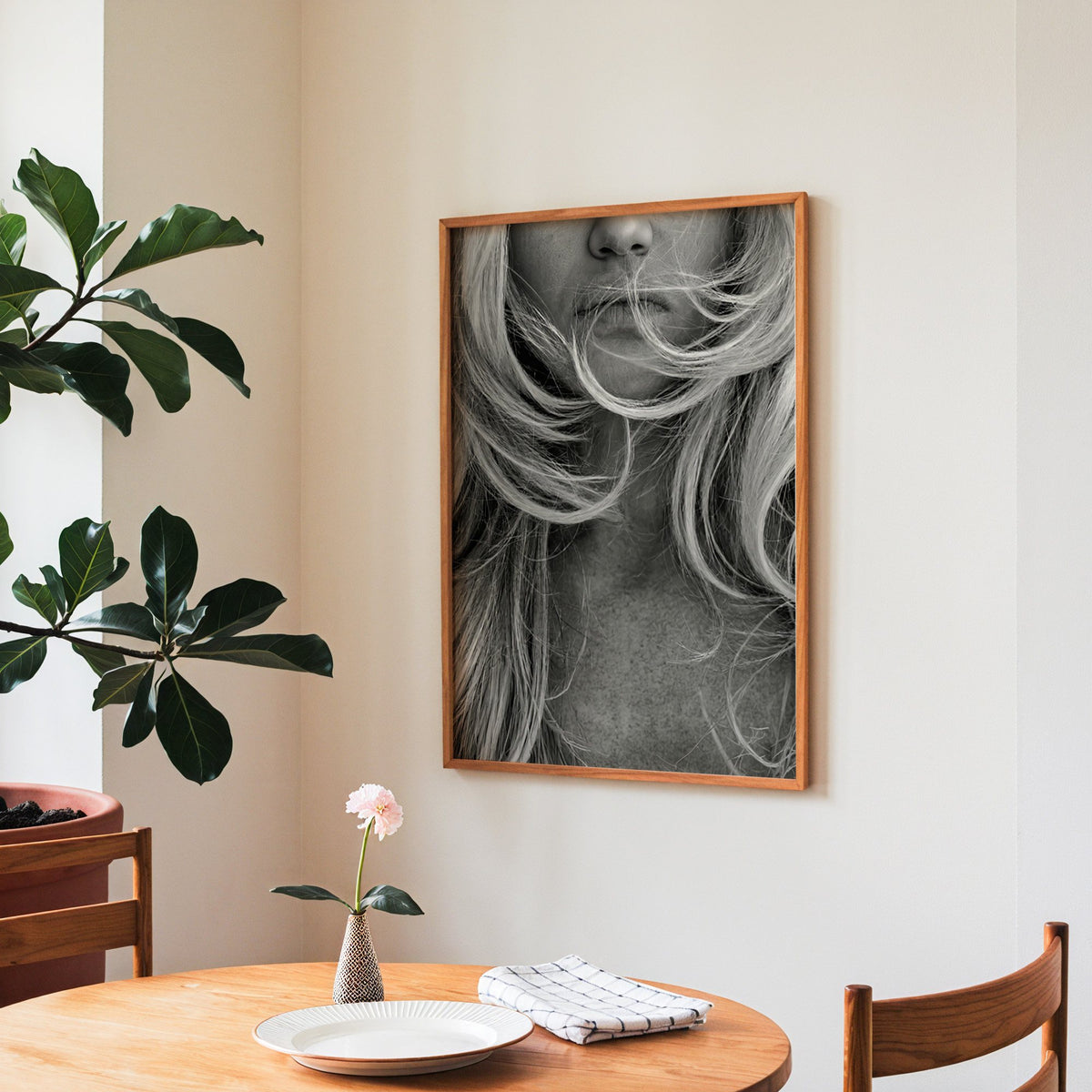 Windswept blonde hair over lips closeup print in a teak frame above a round wooden dining table