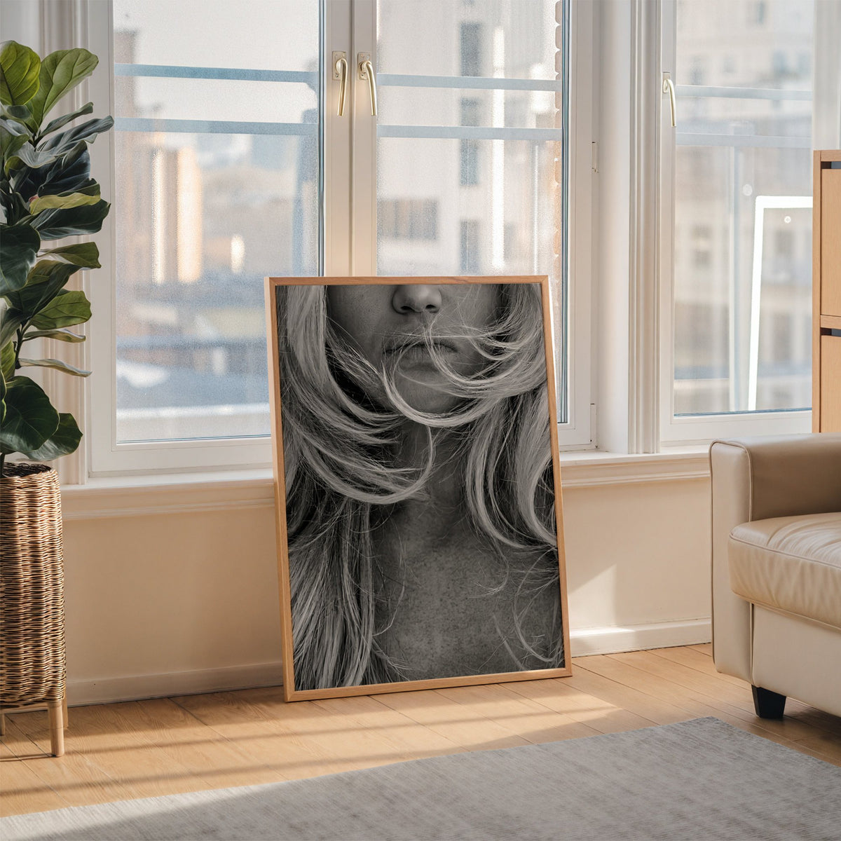 Windswept blonde hair over lips closeup print in an oak frame leaning on the floor beside a fiddle leaf fig