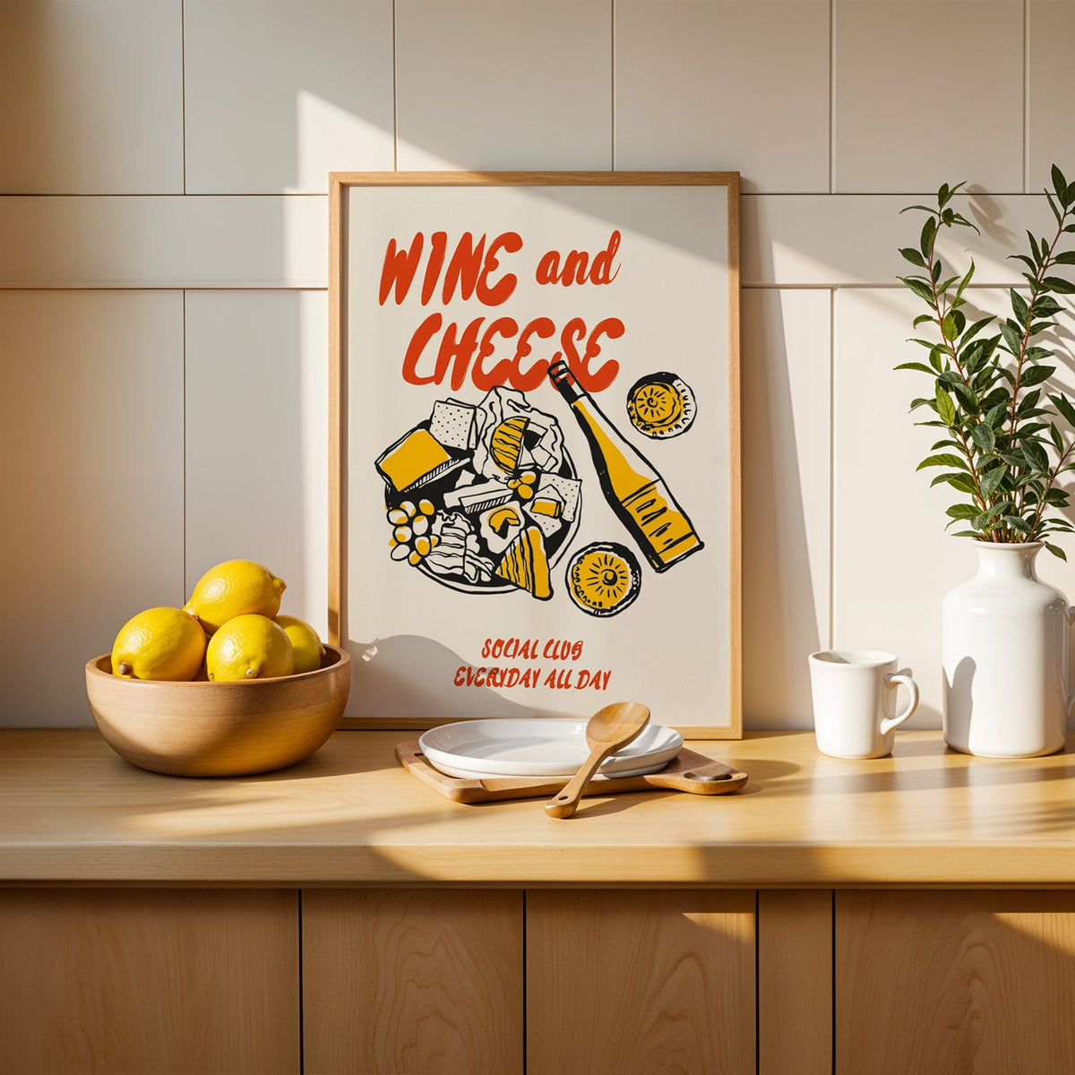 Wine and cheese poster in an oak frame on a kitchen counter beside a wooden bowl of lemons