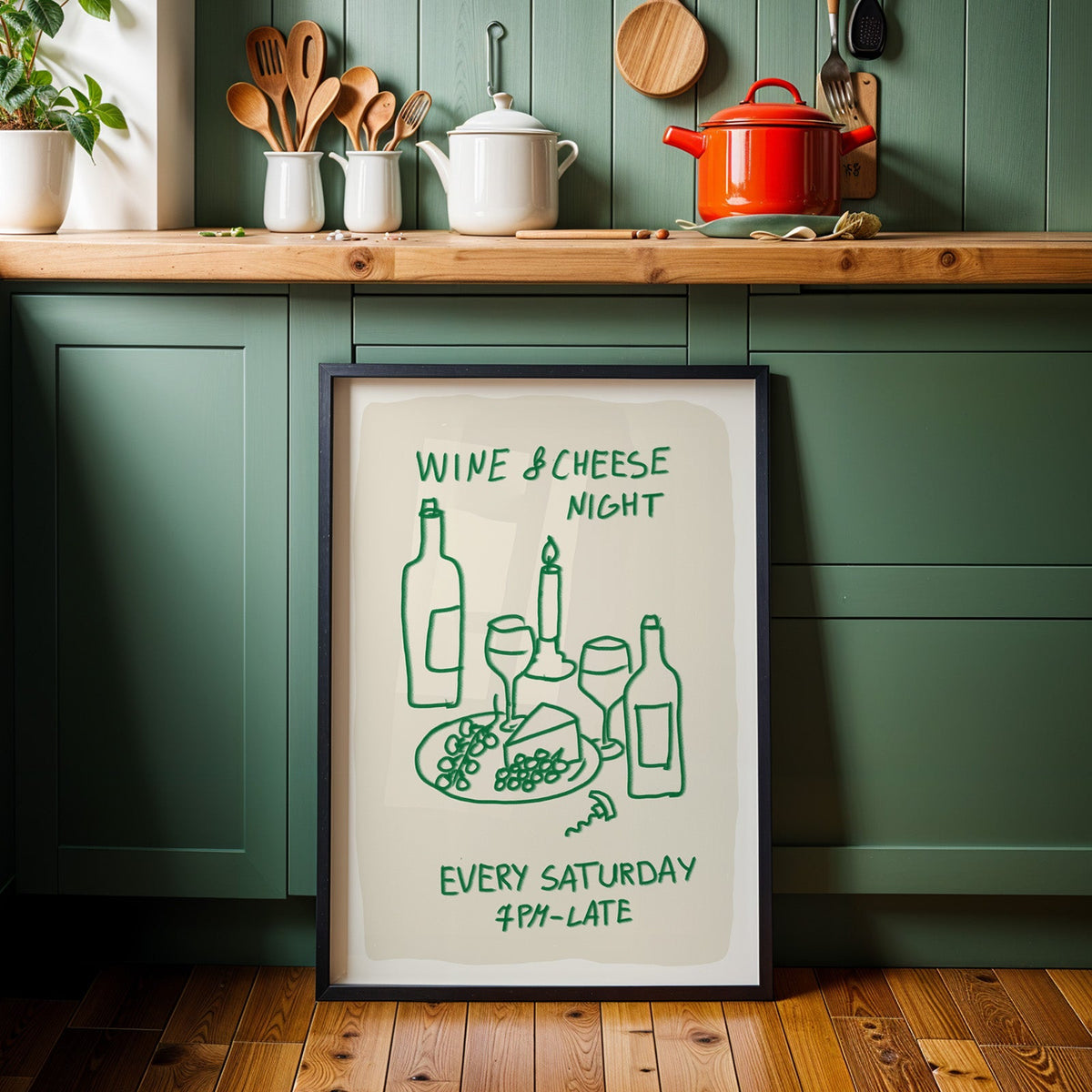 Wine and cheese night print in a black frame against sage green kitchen cabinets