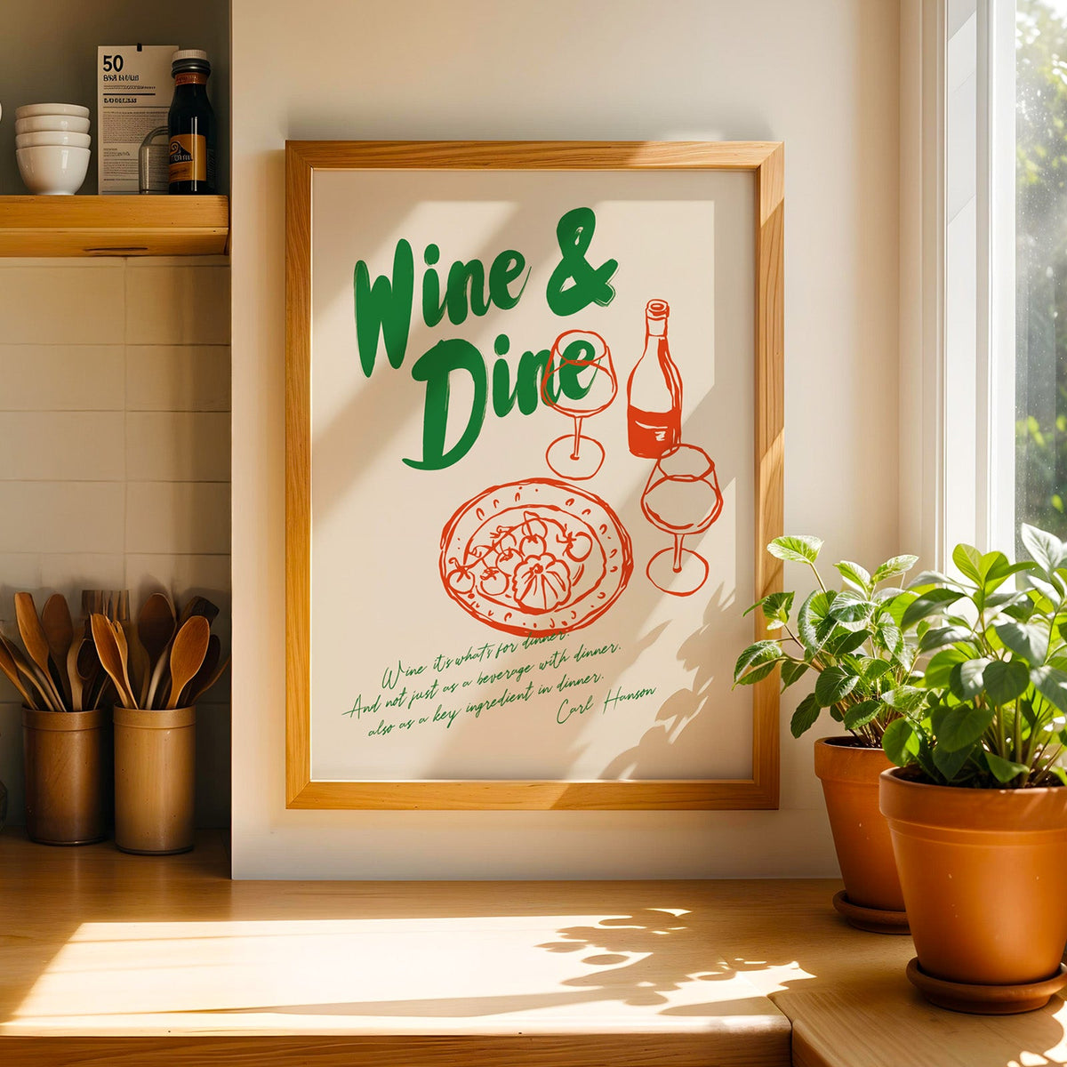 Wine and Dine pizza print in a light pine frame beside a ceramic jar of wooden spoons