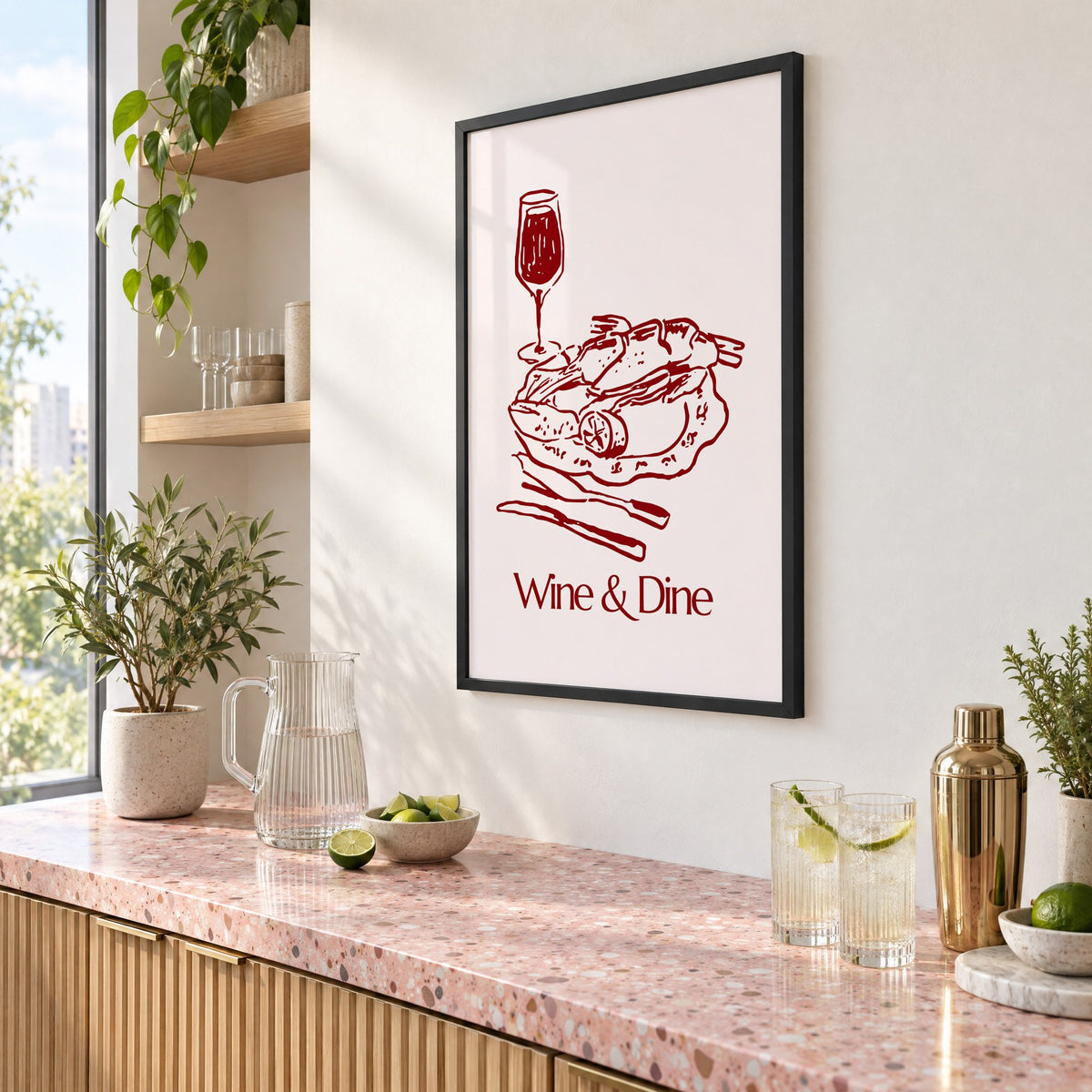 Wine & Dine roast plate burgundy sketch print in a black frame above a pink terrazzo cocktail counter with limes, seen at an angle