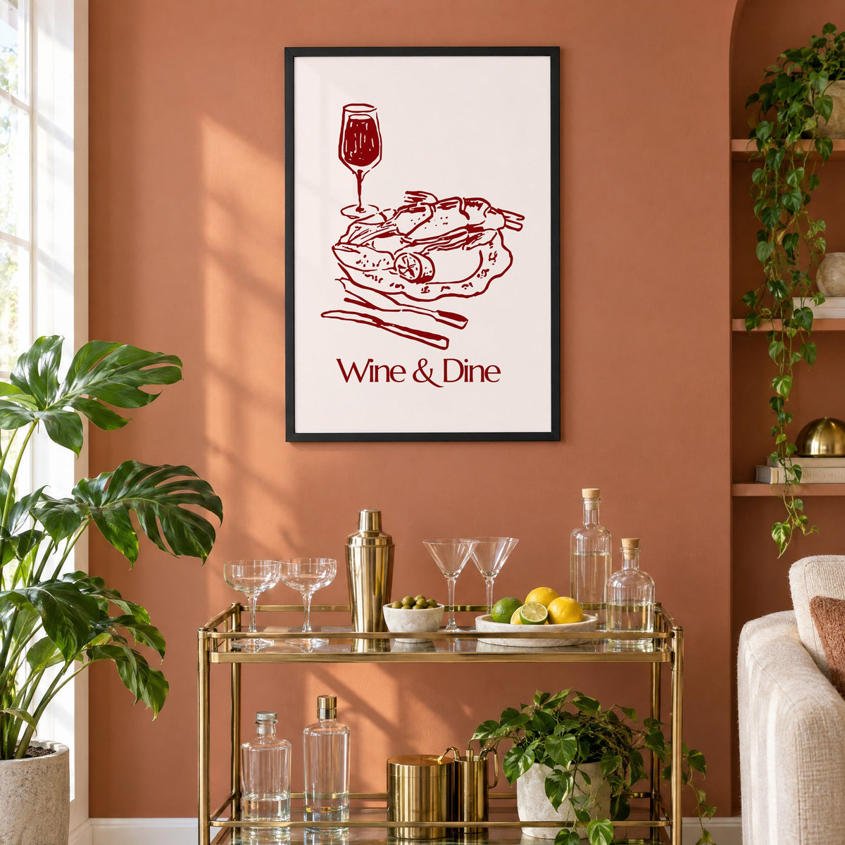 Wine & Dine roast plate burgundy sketch print in a black frame on a terracotta wall above a brass bar cart with coupes and citrus