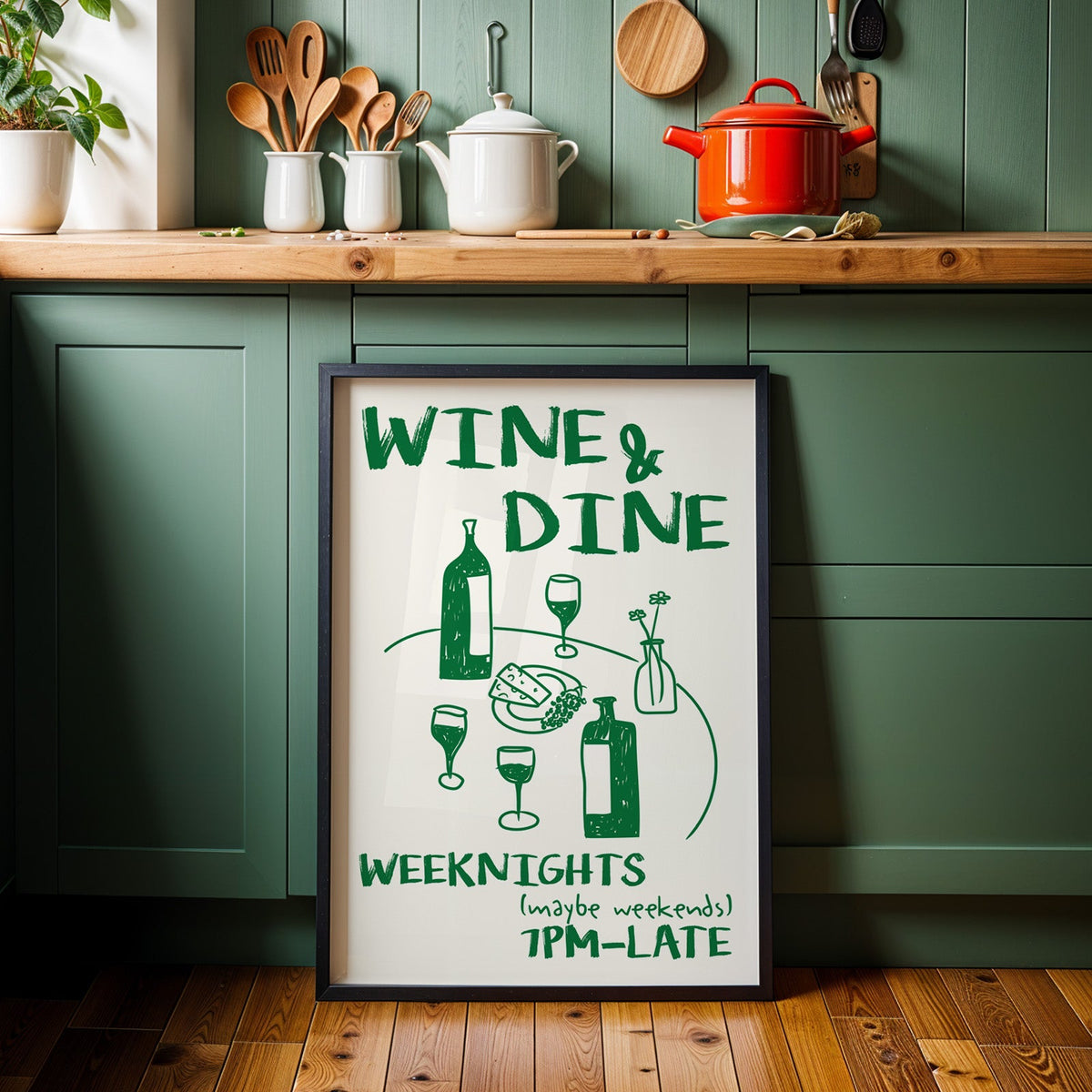 Wine and dine table print in a black frame against sage green kitchen cabinets