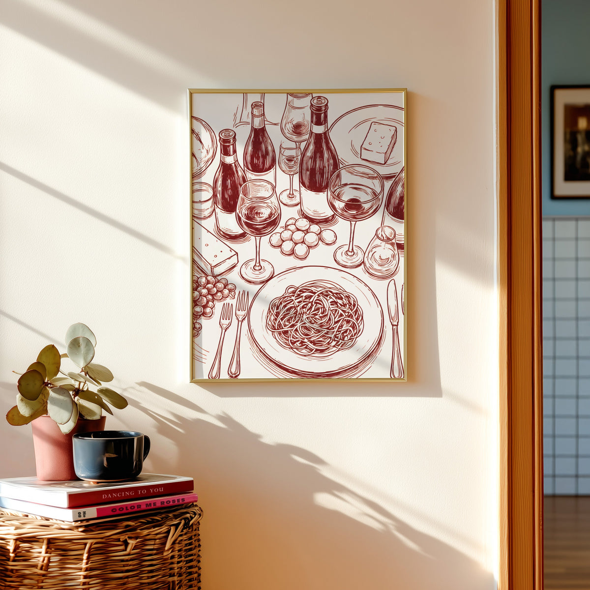 Wine and pasta print shown in a gold frame above a basket of books and a pilea plant