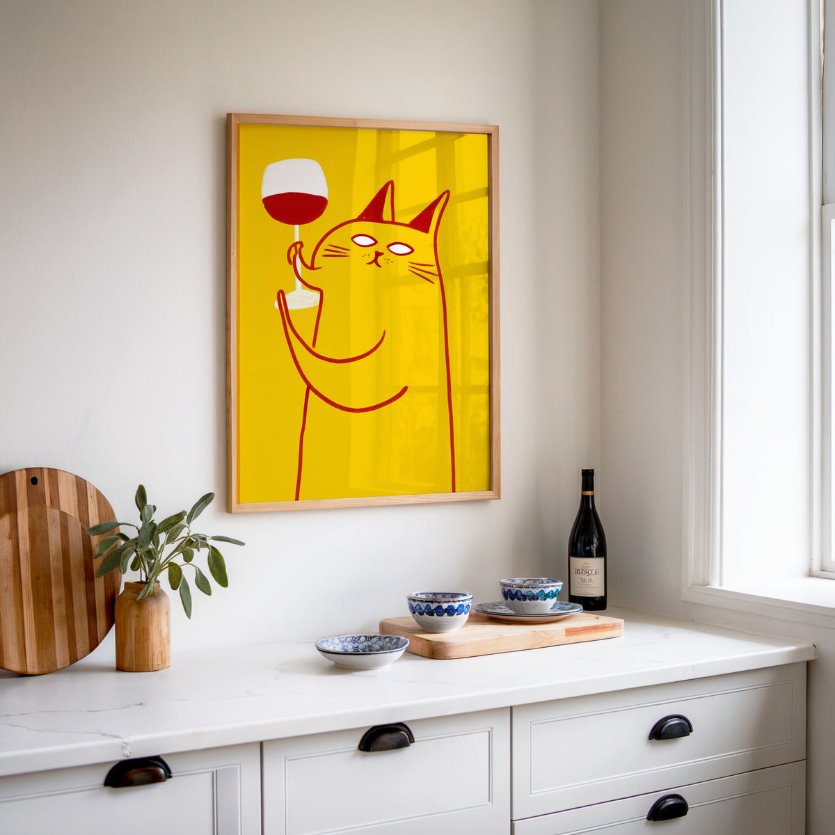 Wine Cat print in an oak frame above a white sideboard with a bottle of wine