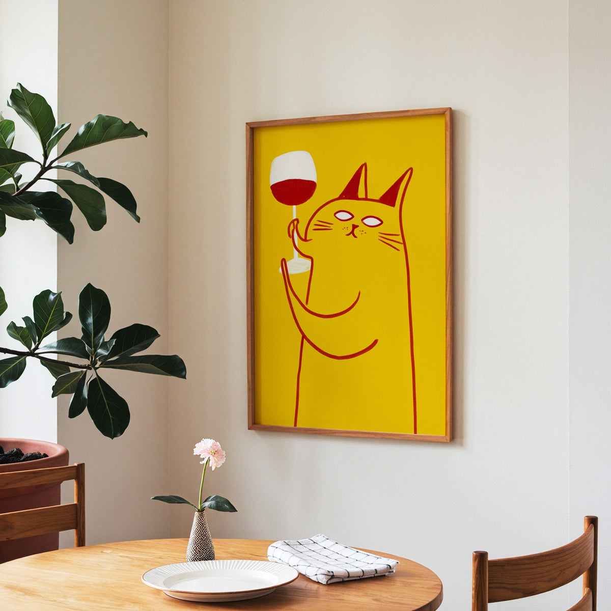 Wine Cat print in a walnut frame above a round table beside a fiddle-leaf fig