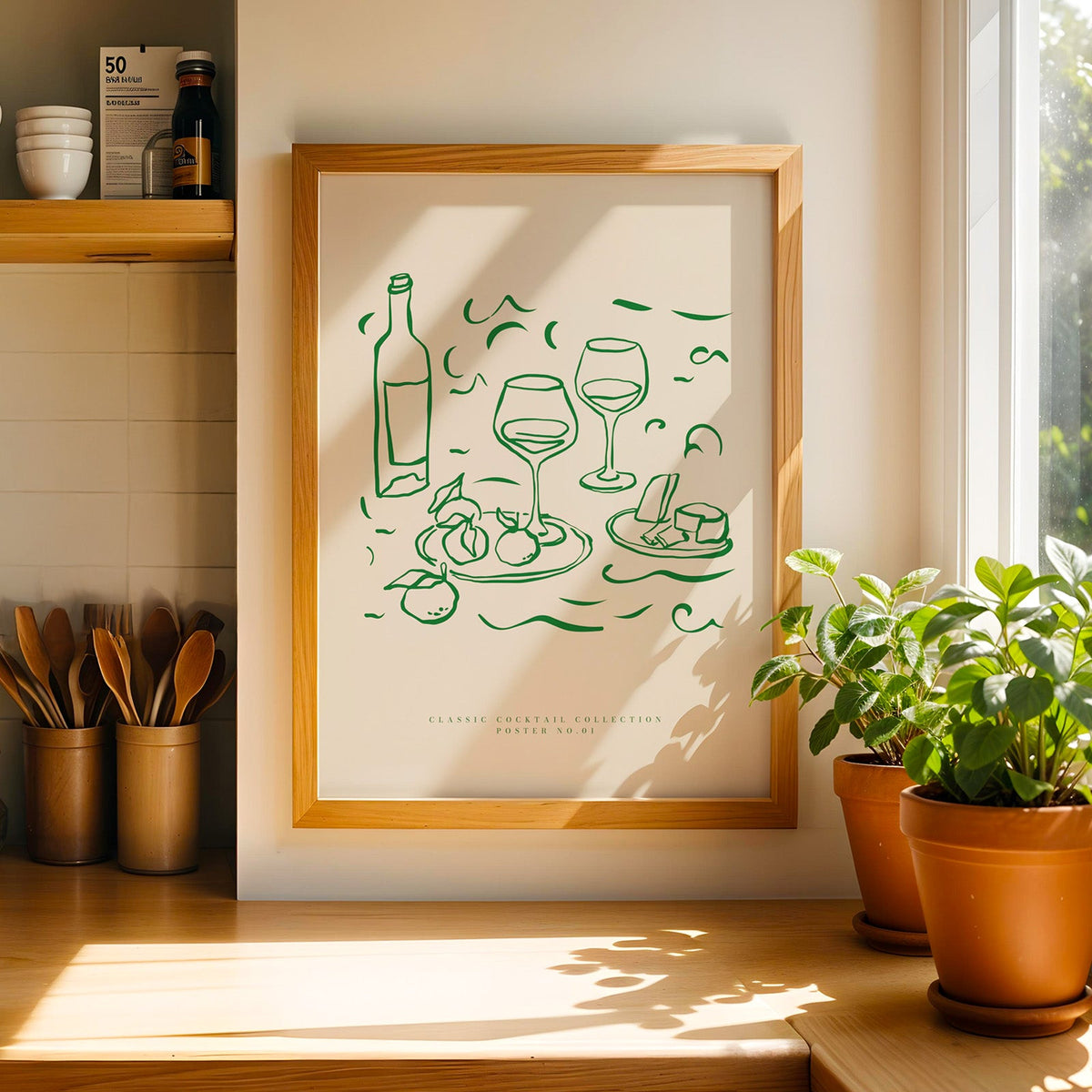 Green line wine and cheese print in a light pine frame beside a jar of wooden spoons
