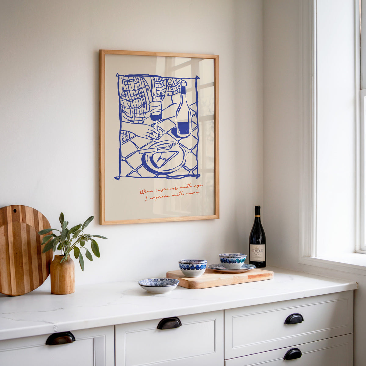 Wine Improves With Age print in an oak frame above a white kitchen sideboard