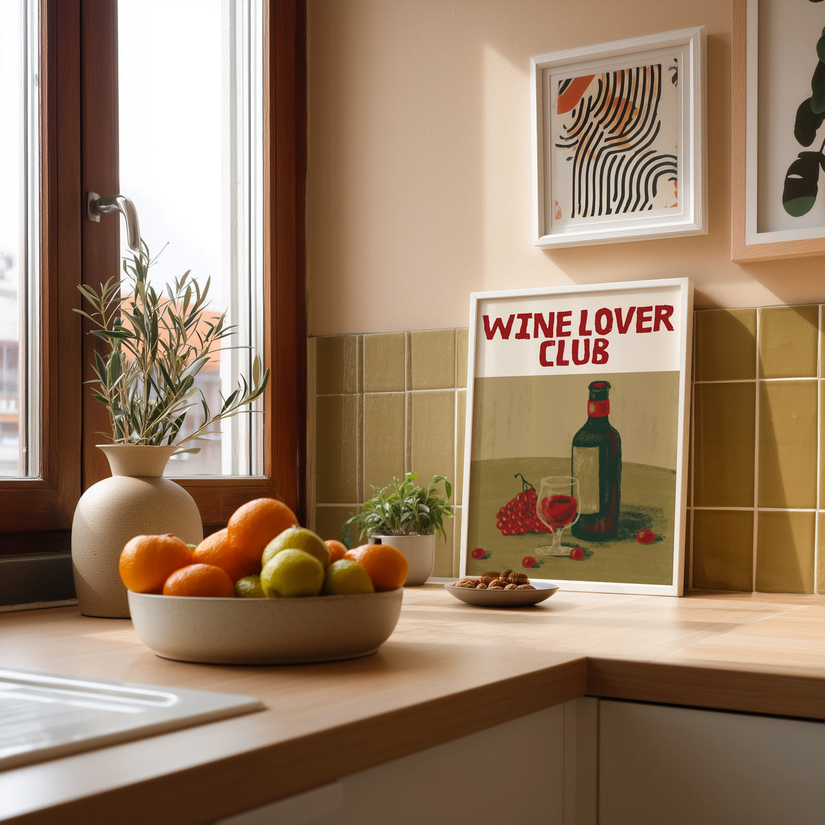 Wine Lover Club bottle and grapes print in a white frame leaning against olive green kitchen tiles beside a bowl of citrus