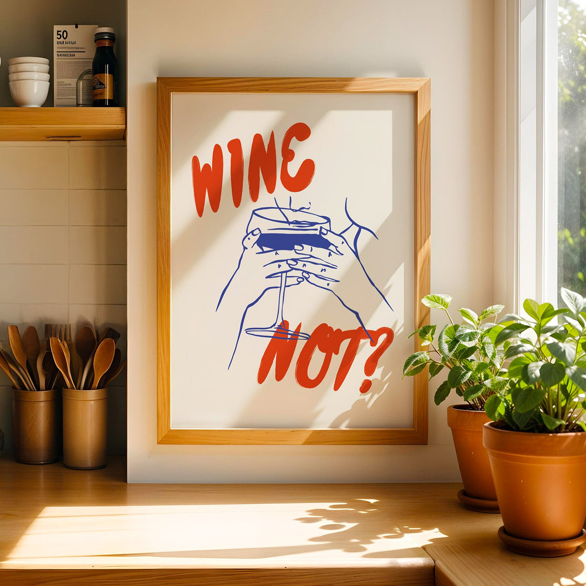 Wine Not print in a light pine frame beside a ceramic jar of wooden spoons