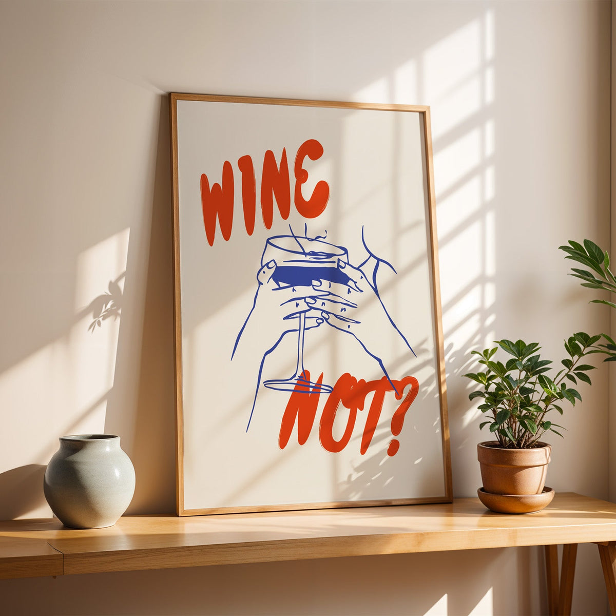 Wine Not print in a slim oak frame on a console with a grey-blue vase