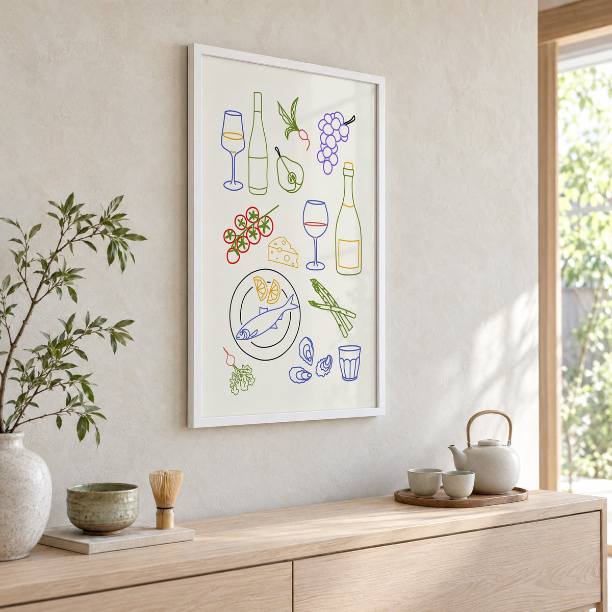 Colorful wine picnic line art print in a white frame above a pale wood console with a matcha tea set