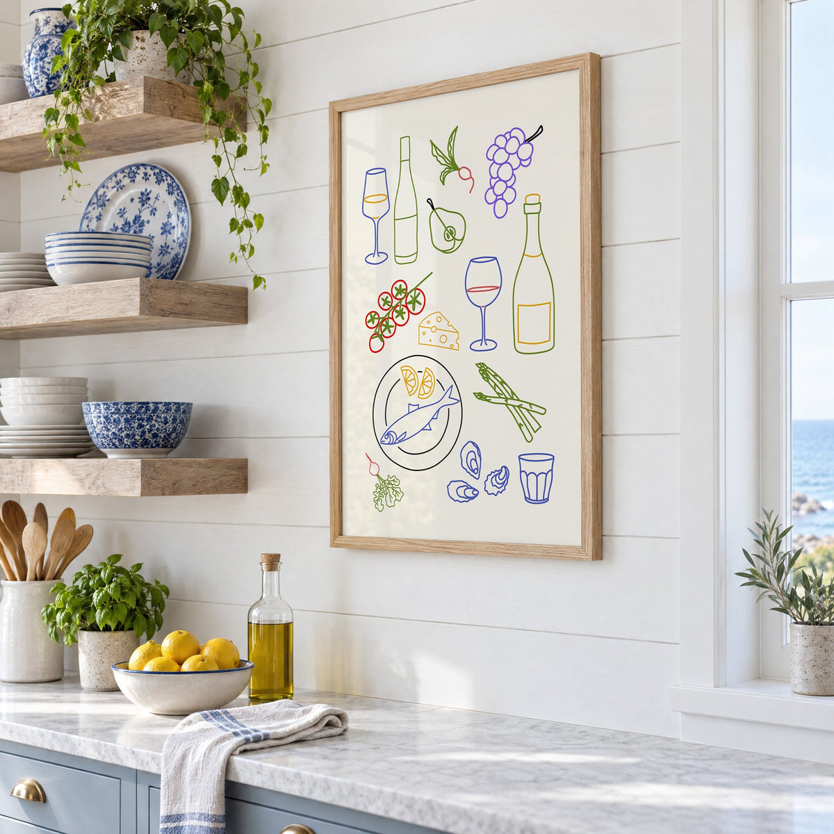 Colorful wine picnic line art print in an oak frame in a white coastal kitchen beside blue and white plates
