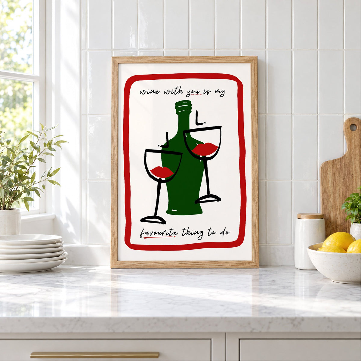 Wine with you lip glasses print in an oak frame leaning on a marble counter by white tiles and lemons