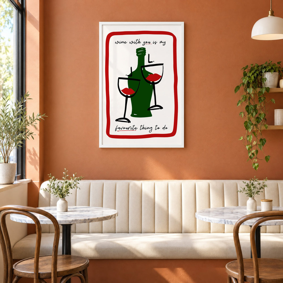 Wine with you lip glasses print in a white frame above a cream banquette on a terracotta cafe wall