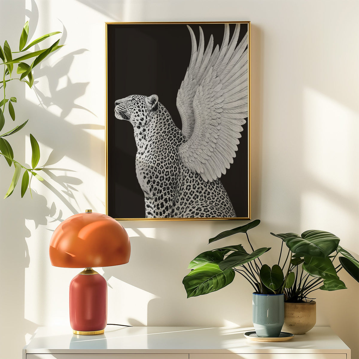 Winged leopard on black background print shown in a gold frame above a white sideboard with an orange lamp