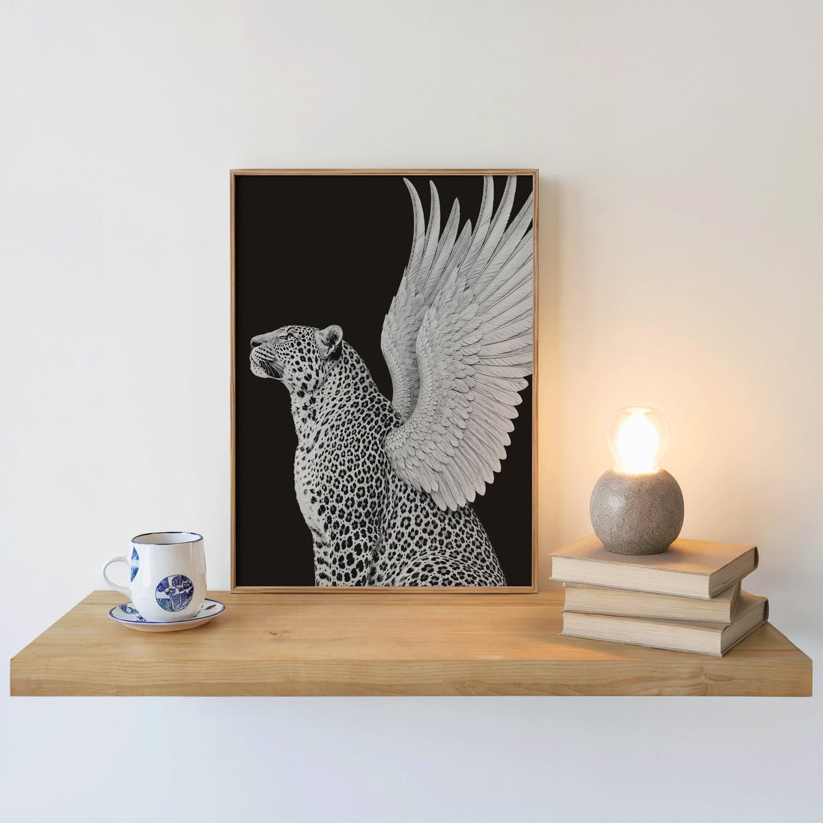 Winged leopard on black background print in an oak frame on a floating shelf beside a glowing lamp
