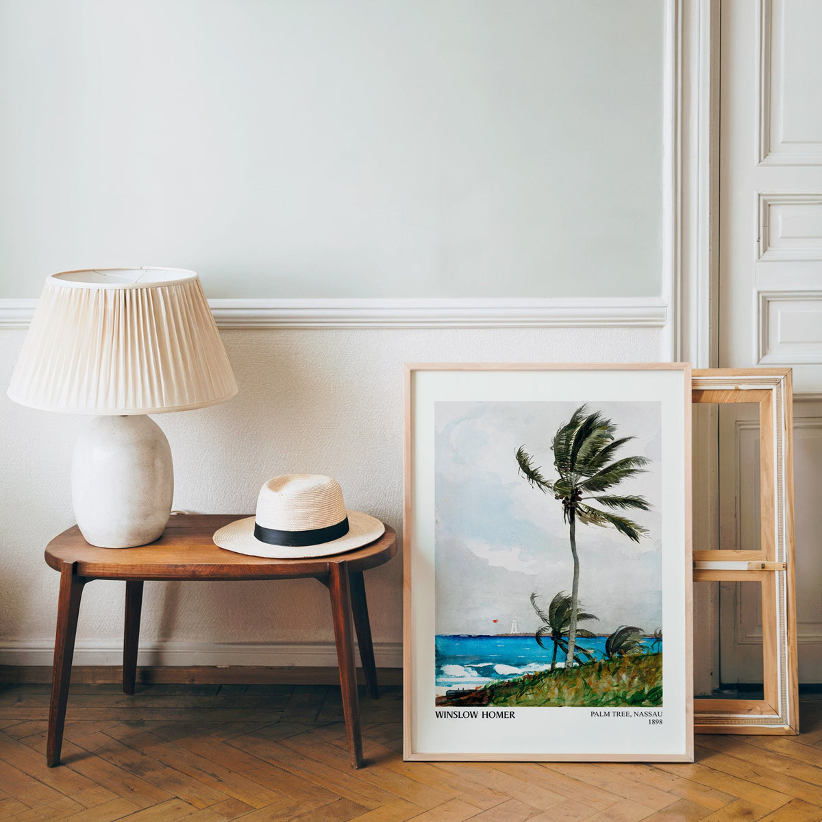 Coastal watercolour poster in a light wood frame leaning by a bench and hat