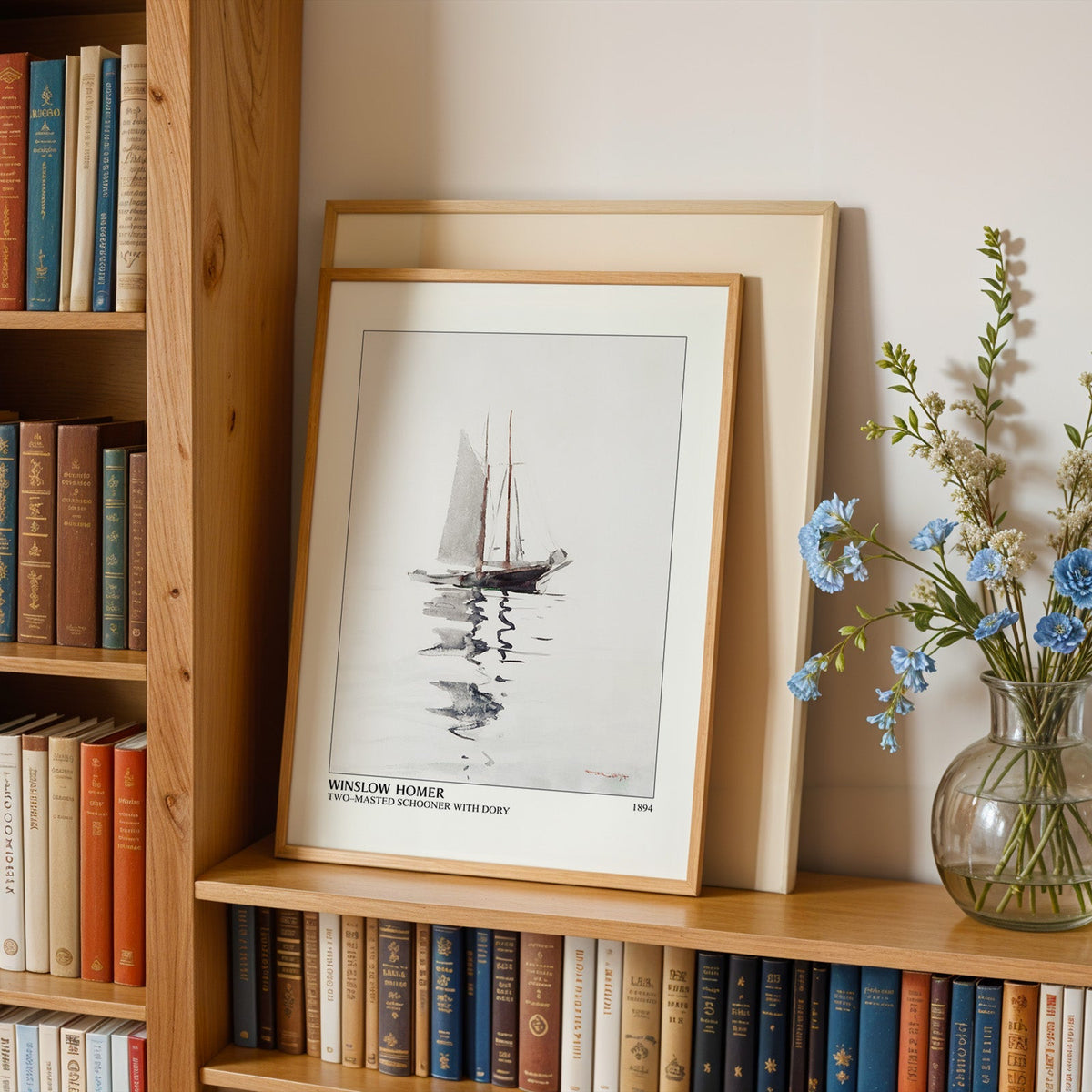 Schooner print in an oak frame leaning on a bookshelf beside blue flowers