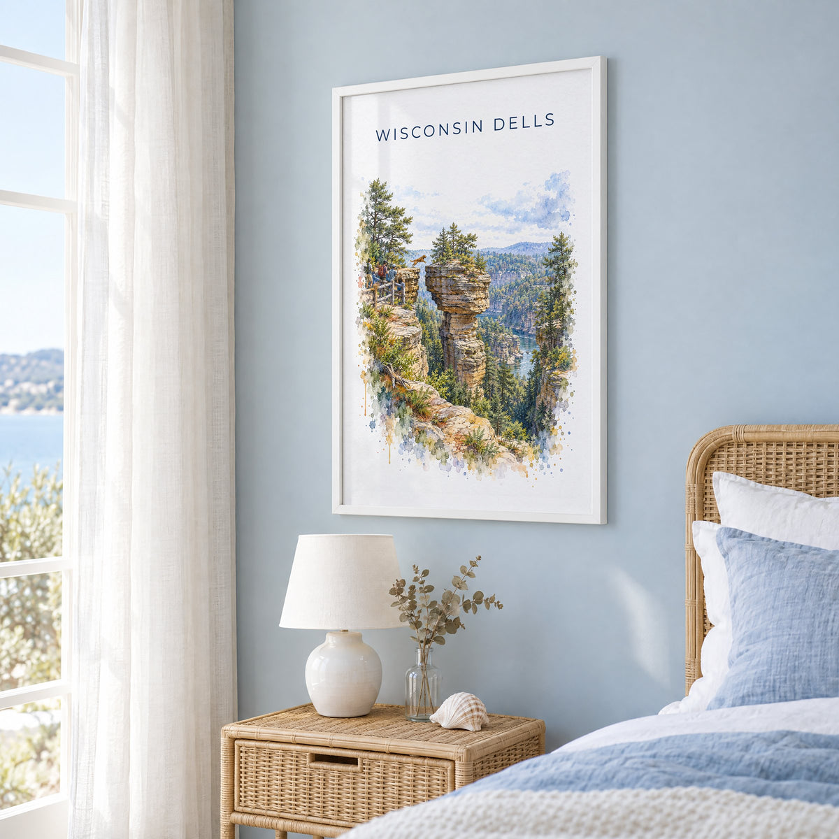 Wisconsin Dells watercolor print in a white frame on a pale blue wall beside a rattan bed in a coastal bedroom