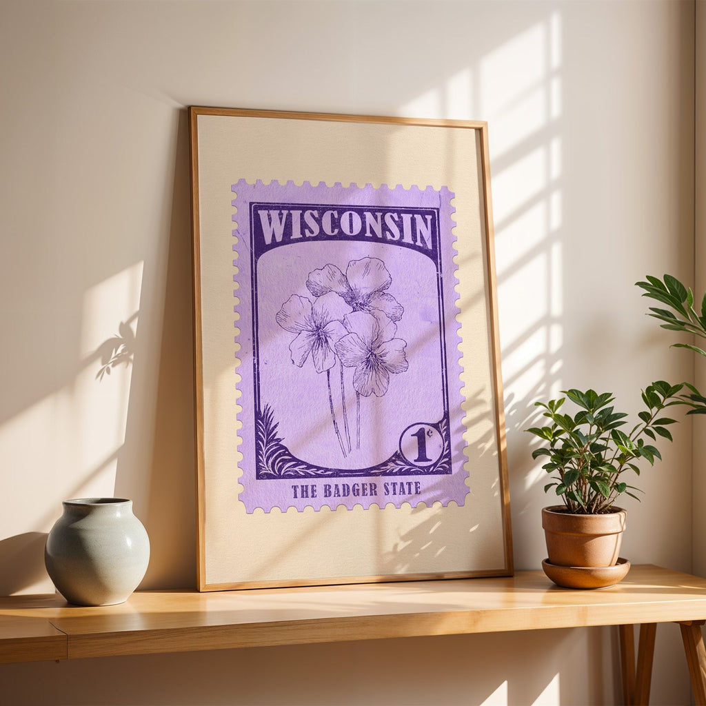 Wisconsin Wood Violet stamp print in a light oak frame leaning on a wooden table beside a stoneware vase