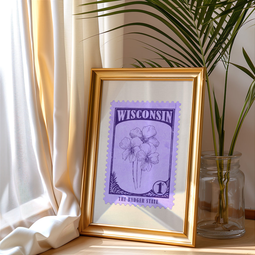 Wisconsin stamp print in a gold frame leaning by a cream curtain with a palm in a glass jar