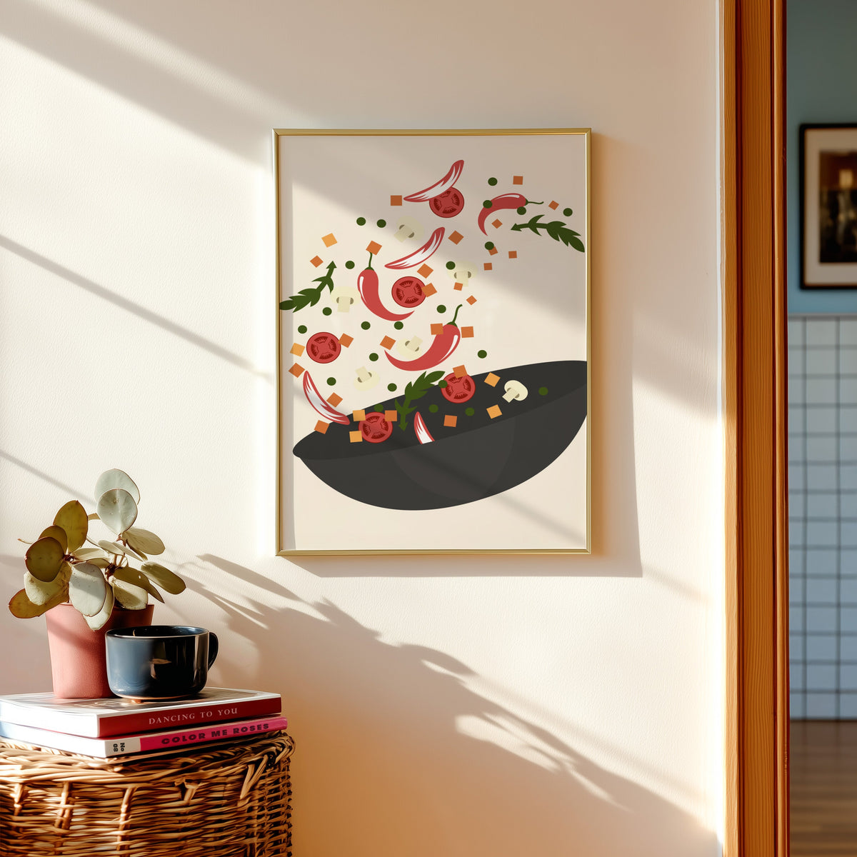 Wok toss print shown in a gold frame above a basket of books and a pilea plant