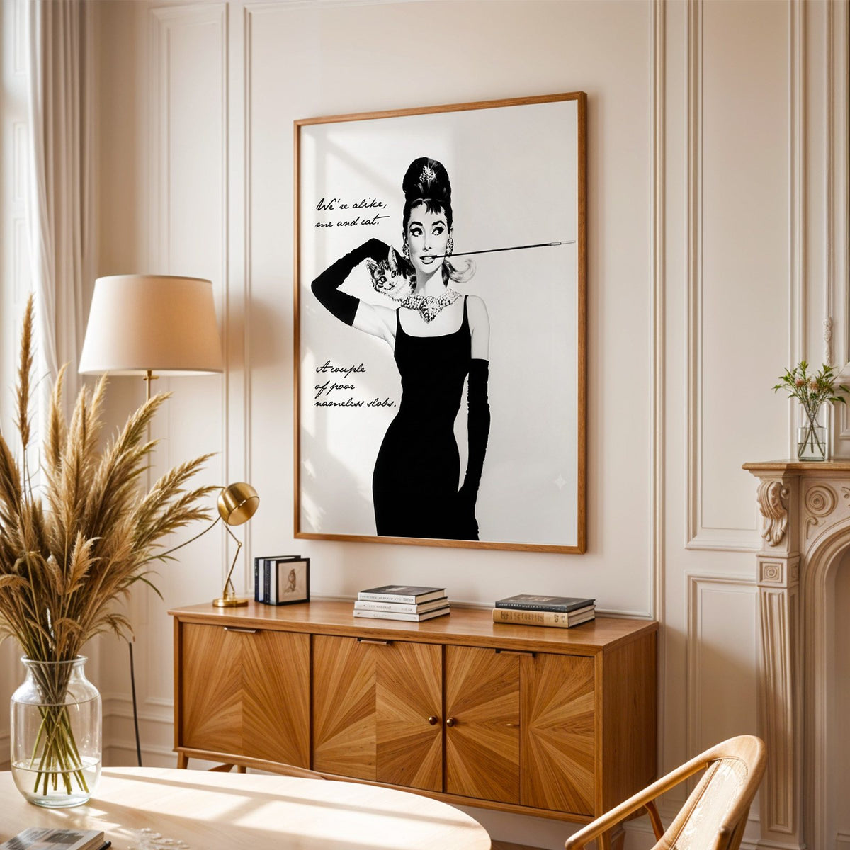 Woman in black dress with kitten and handwritten quote print in an oak frame above a sunburst wood sideboard with pampas grass