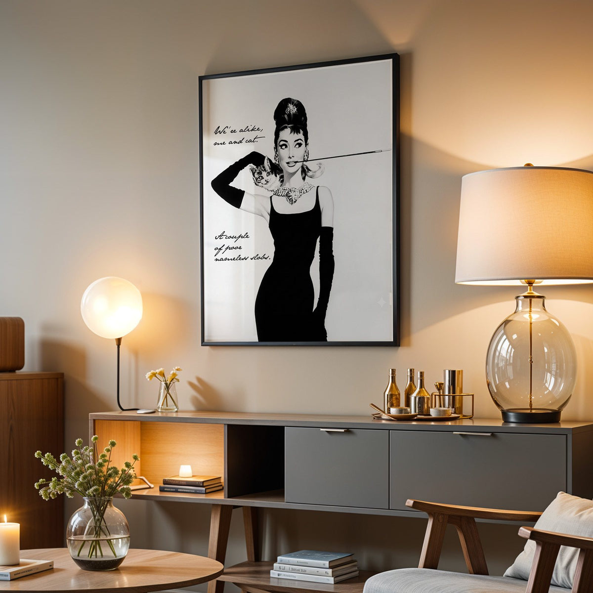 Woman in black dress with kitten and handwritten quote print in a black frame above a grey media console with a glass table lamp