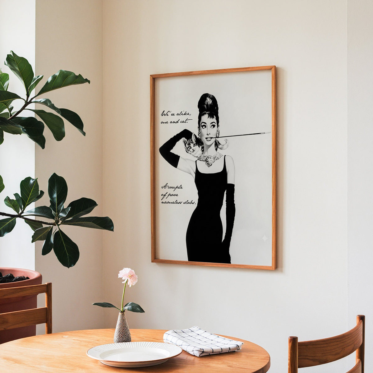 Woman in black dress with kitten and handwritten quote print in a teak frame above a round wooden dining table