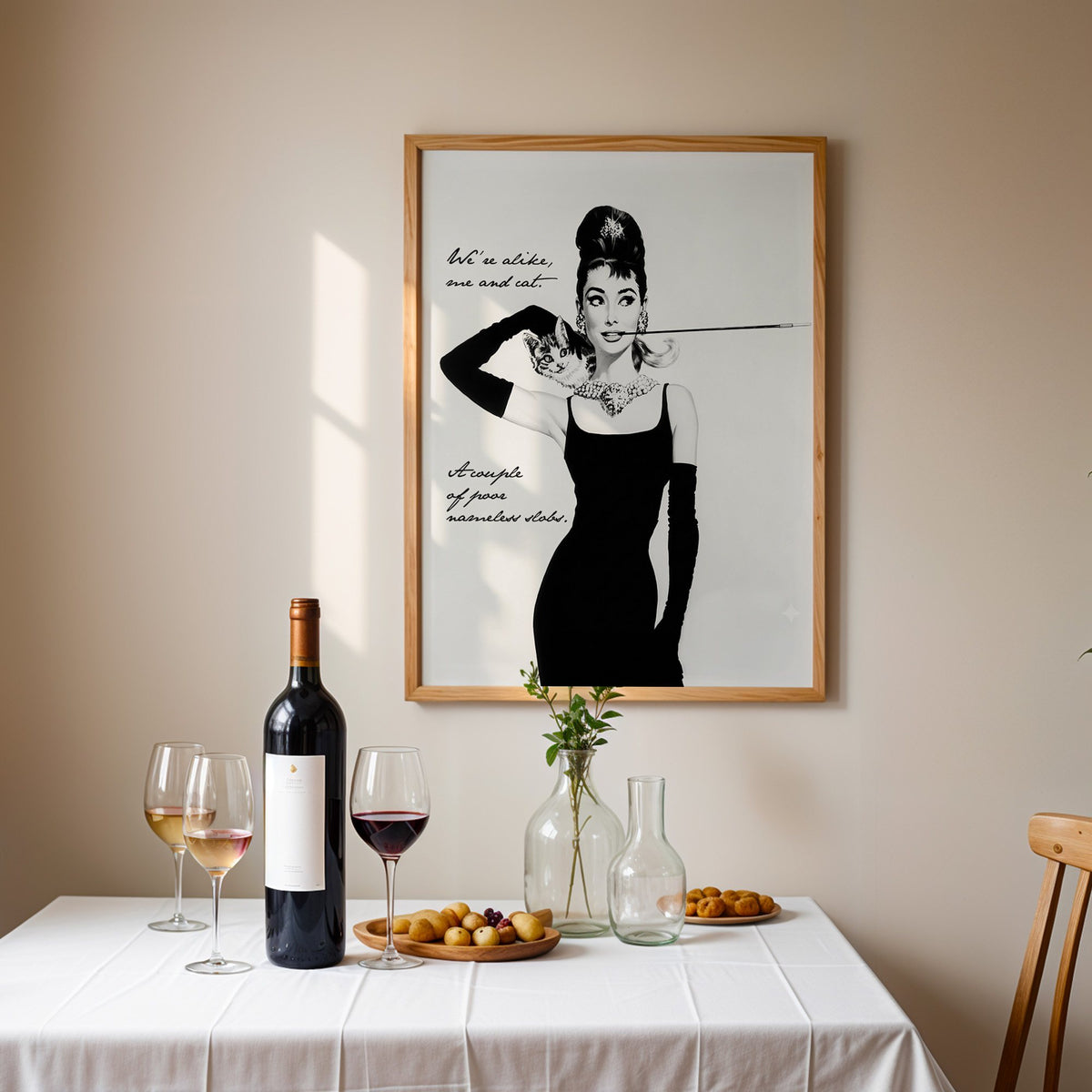 Woman in black dress with kitten and handwritten quote print in an oak frame above a table set with red wine and glasses