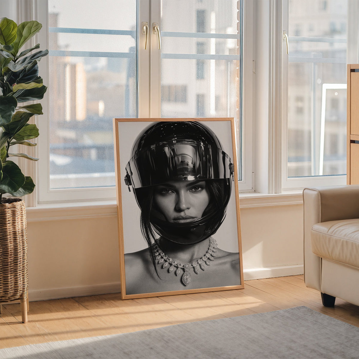 Woman in glossy black helmet and diamond necklace print in an oak frame leaning on the floor beside a fiddle leaf fig