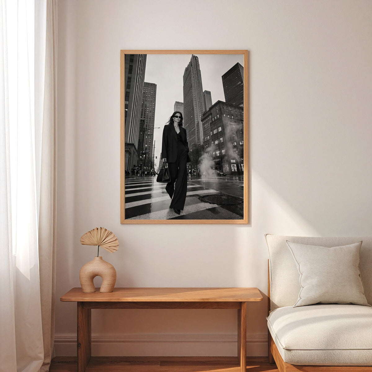 Woman in black suit on New York crosswalk print in an oak frame above a narrow console with an arched vase